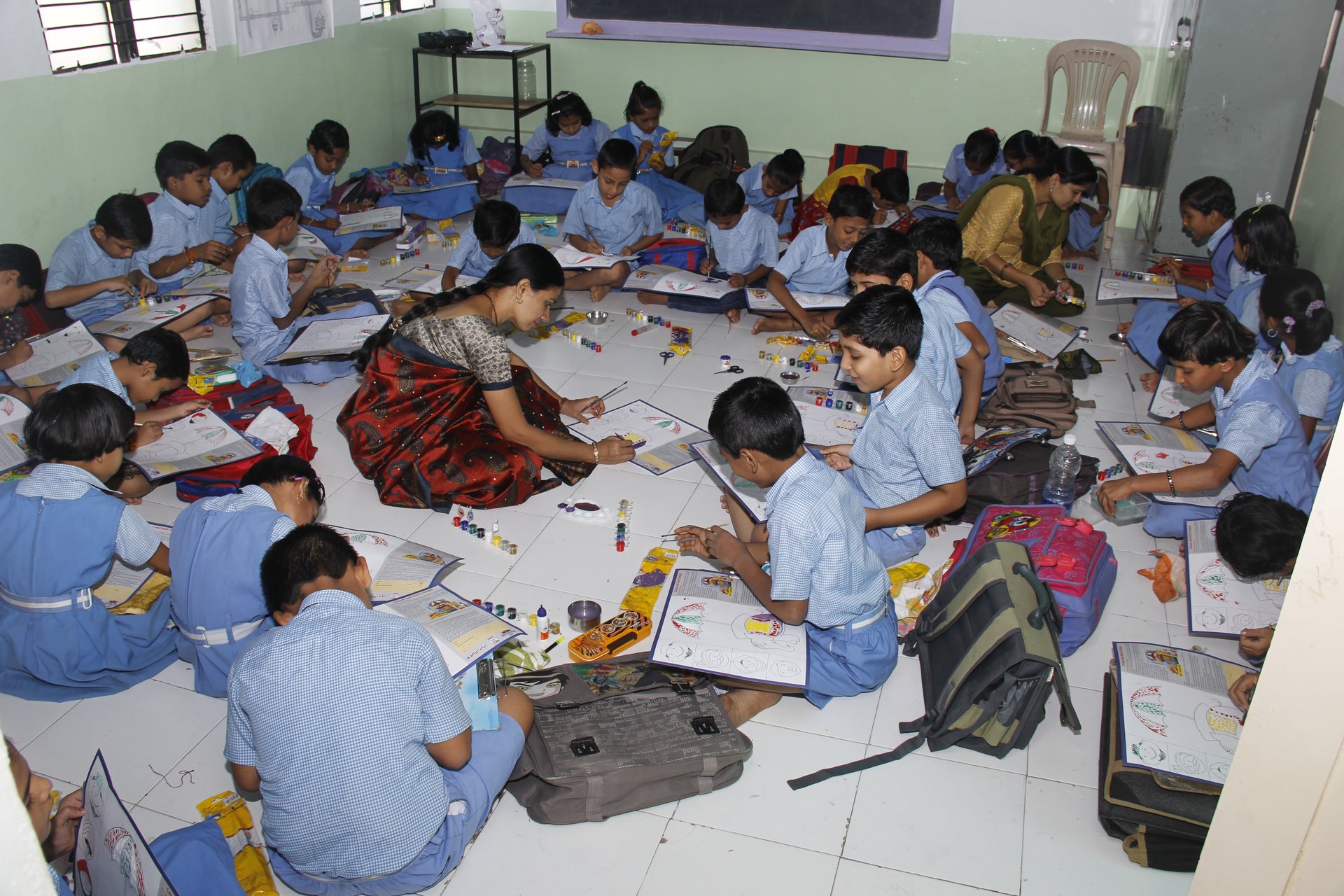 Learning through action — students seated on the classroom floor with their books and drawing materials